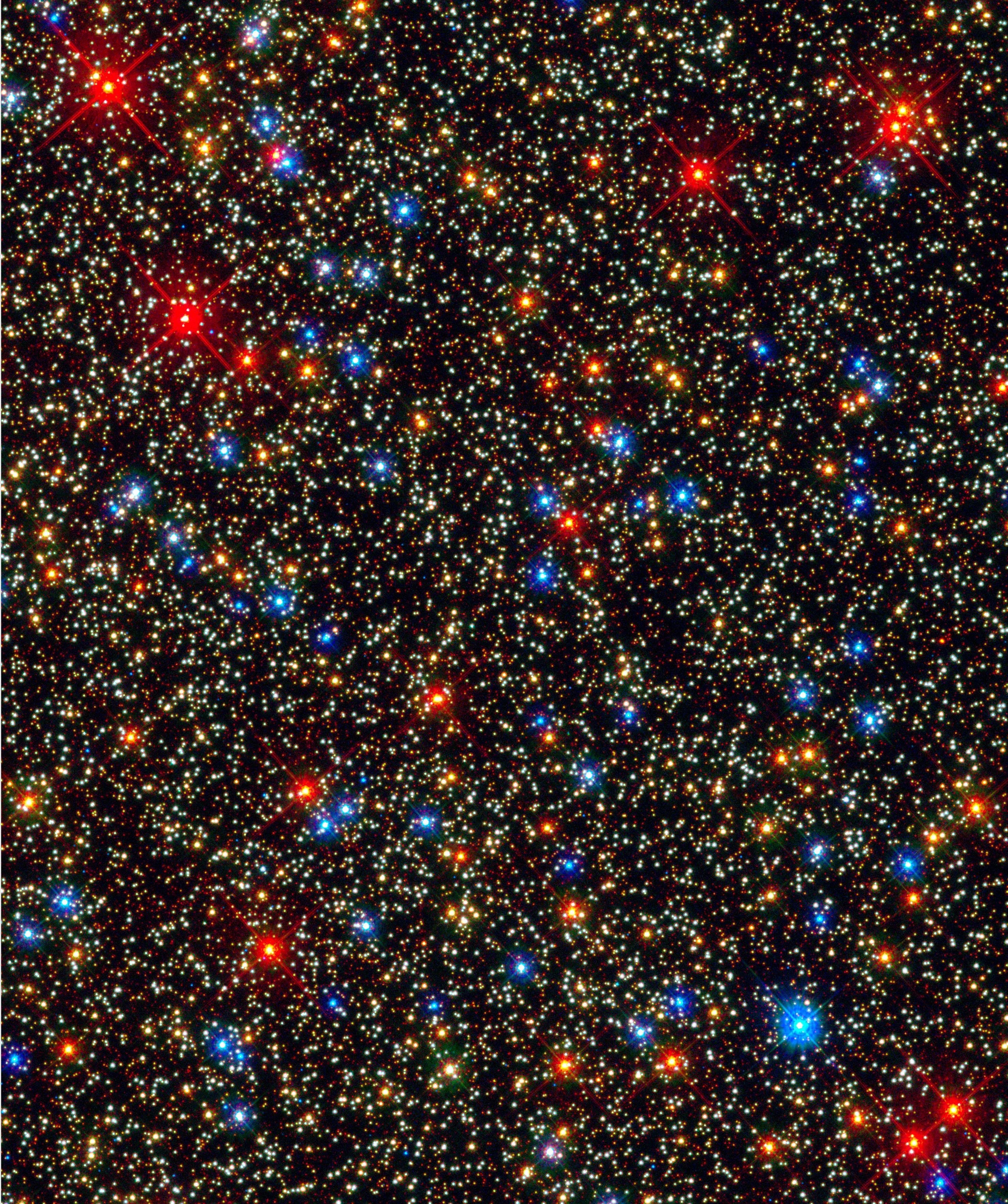 Wide field image of stars with some in white and others in bright yellow blue and red against deep space