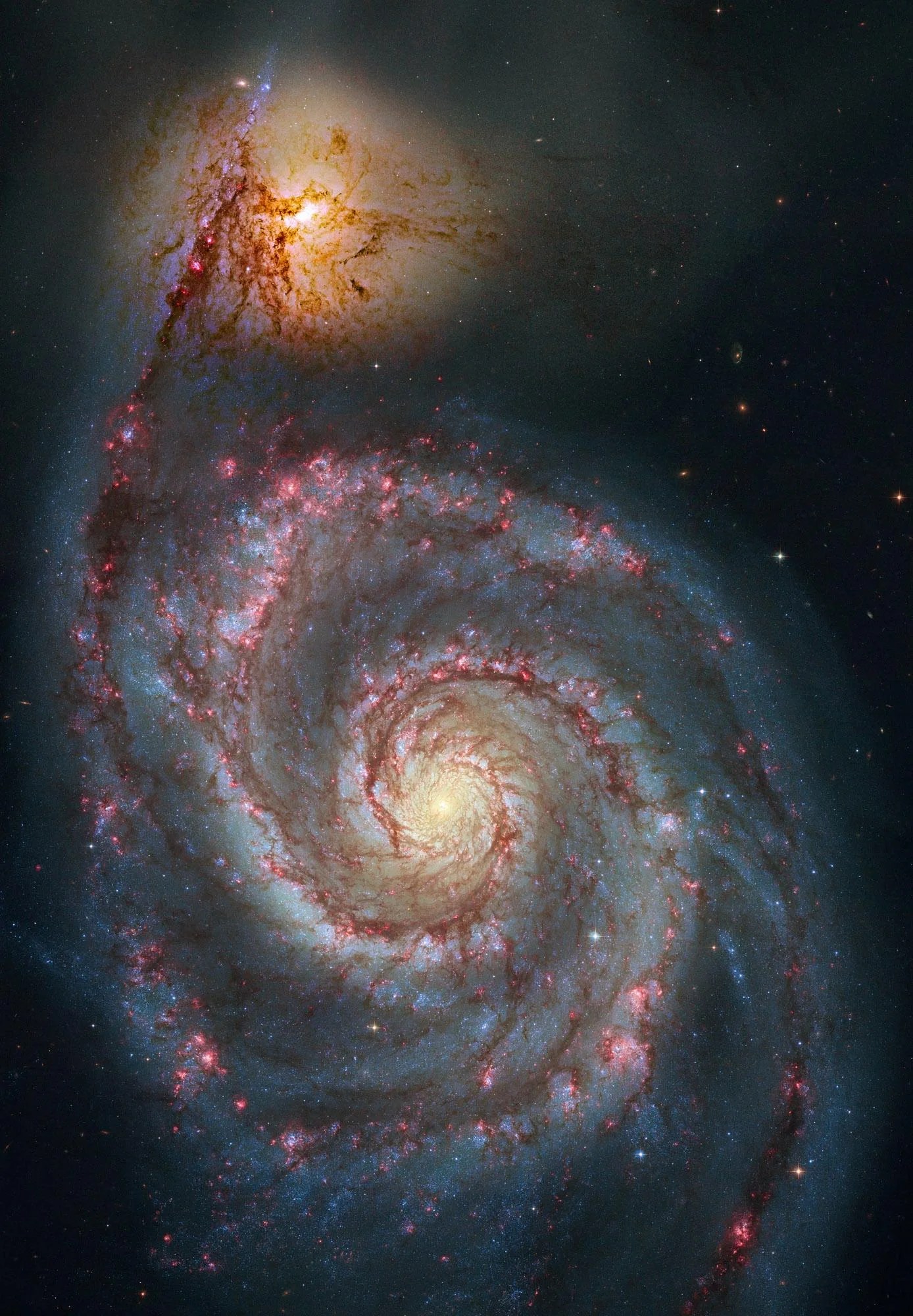 A large, face-on spiral galaxy fills the image. It's bright core is surrounded by pinkish-red dusty spiral arms.