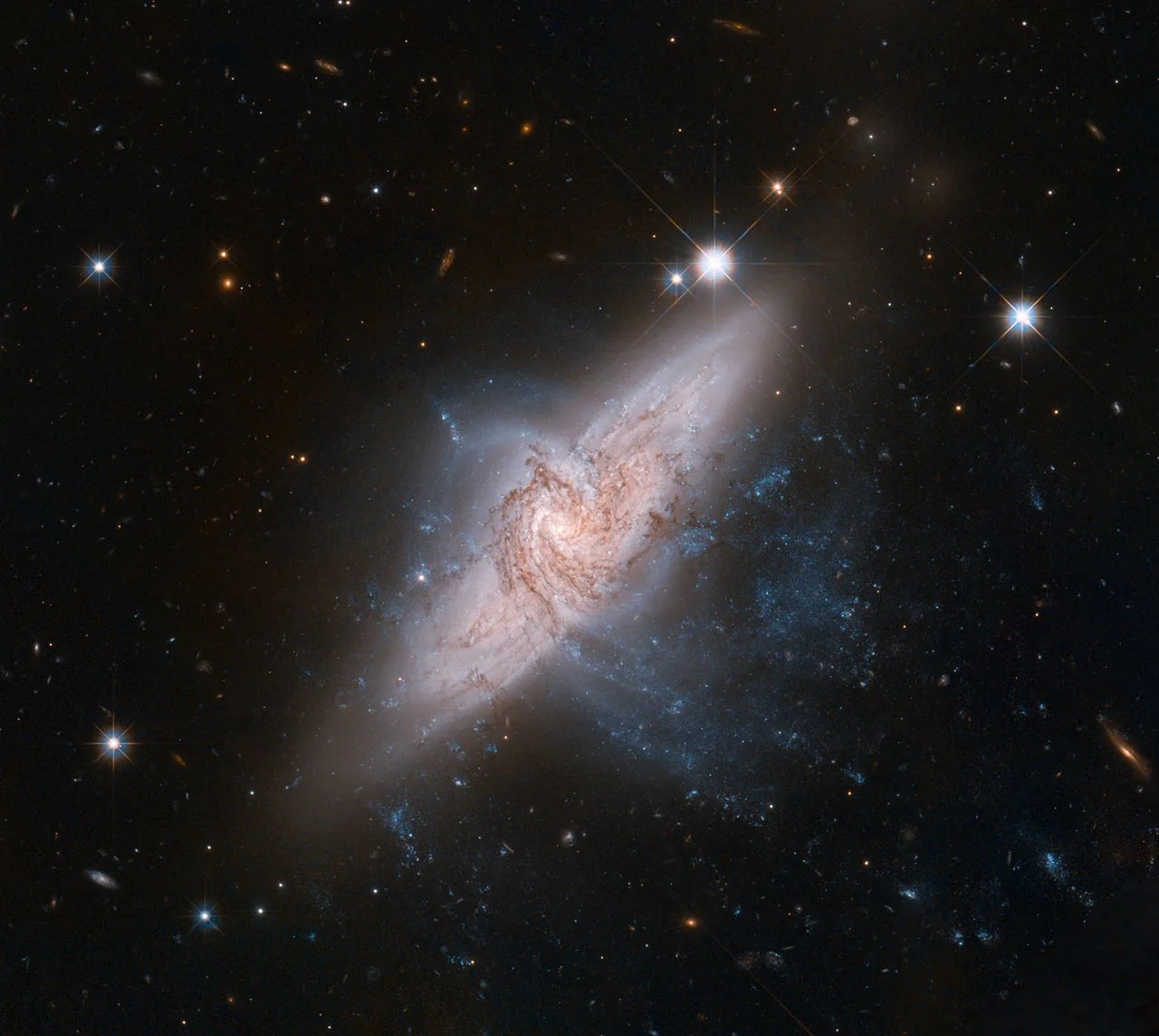 Two edge-on, spiral galaxies appear to be at right angles to each other. One extending from the lower left to the upper right. The other has distinct spiral arms and dust lanes and extends from just left of center to the lower right. Black background dotted with stars.