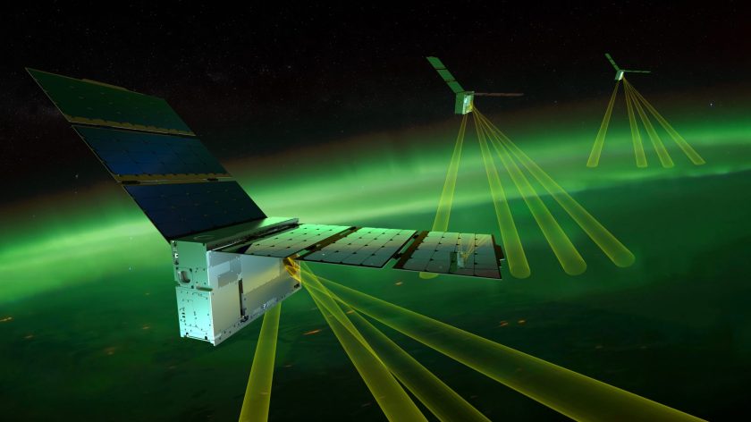 This conceptual illustration shows the three EZIE small satellite missions flying in formation above a beautiful aurora on Earth.