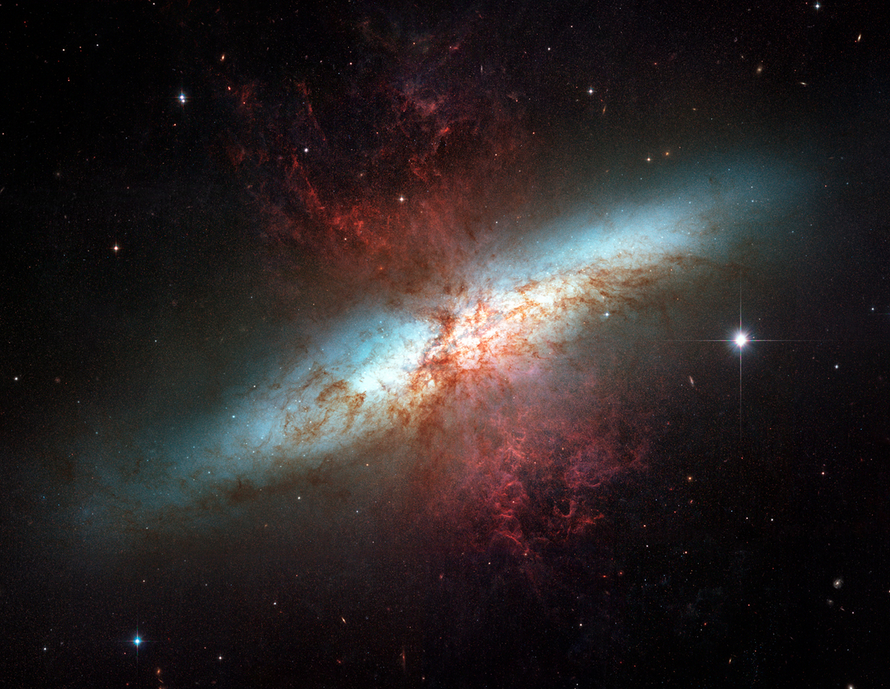 A bluish streak of light extends from the lower left to the upper right, with threads of reddish dust and gas seen throughout, all against a black backdrop of space.