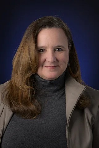 Portrait photo of a smiling woman with long brown hair and wearing dark clothing