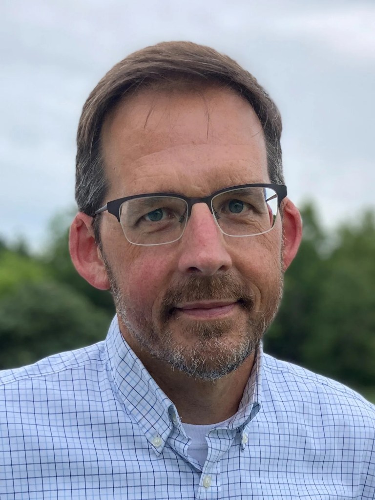 Portrait photo of a man with short brown hair and eye glasses looking to the camera.