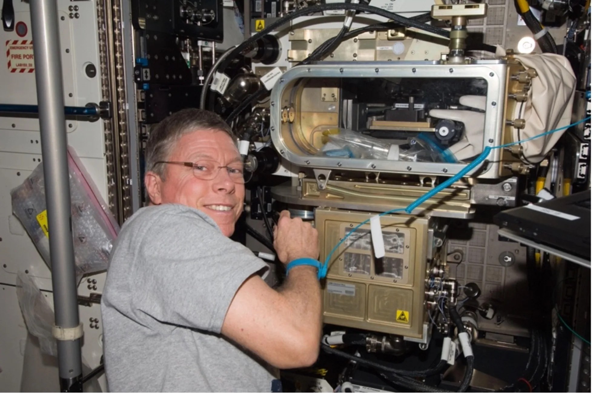 Astronaut in front of a large, gold metallic device with a rectangular glass opening.