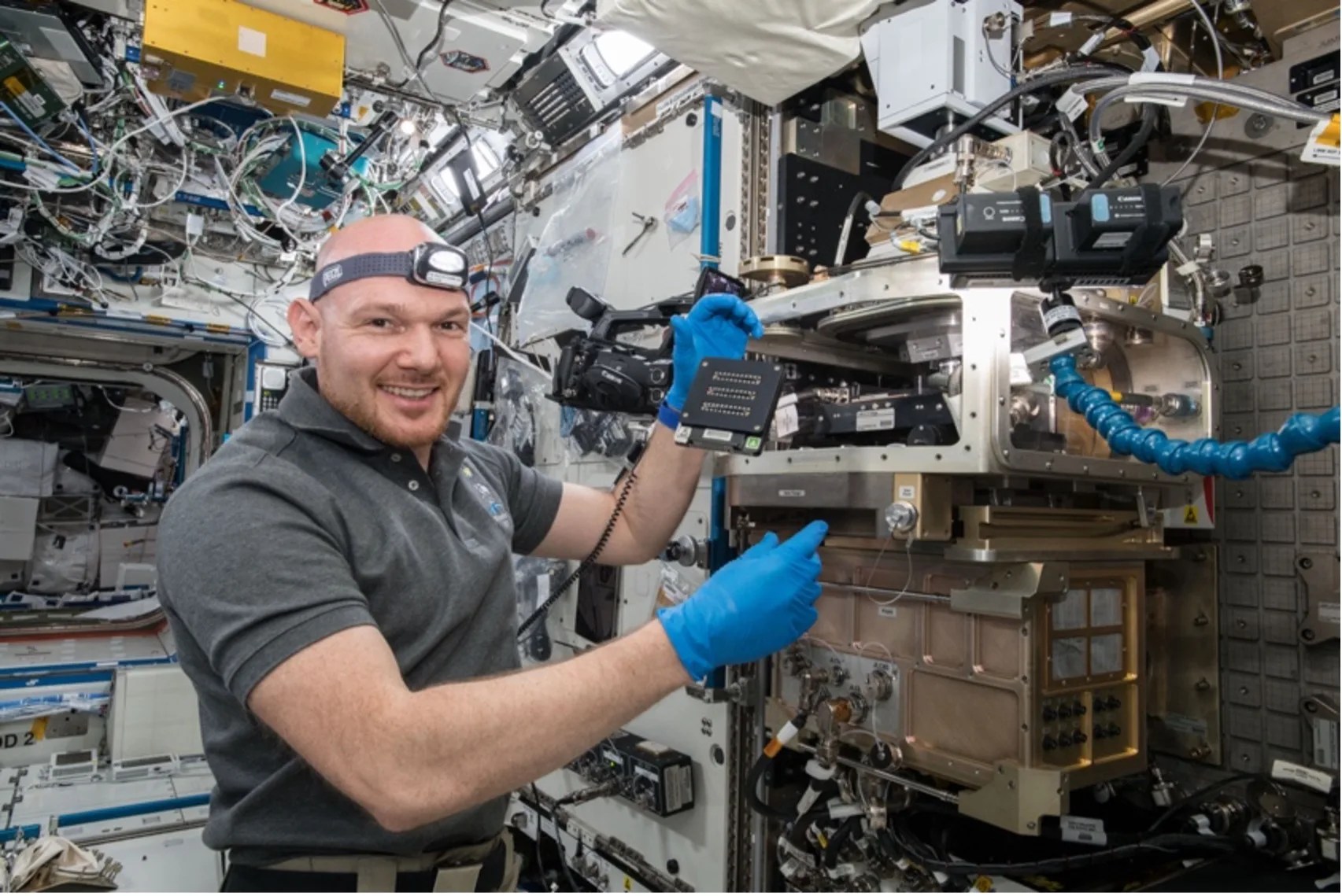 Astronaut in International Space Station with blue latex gloves with floating flat, square device floating between hands.