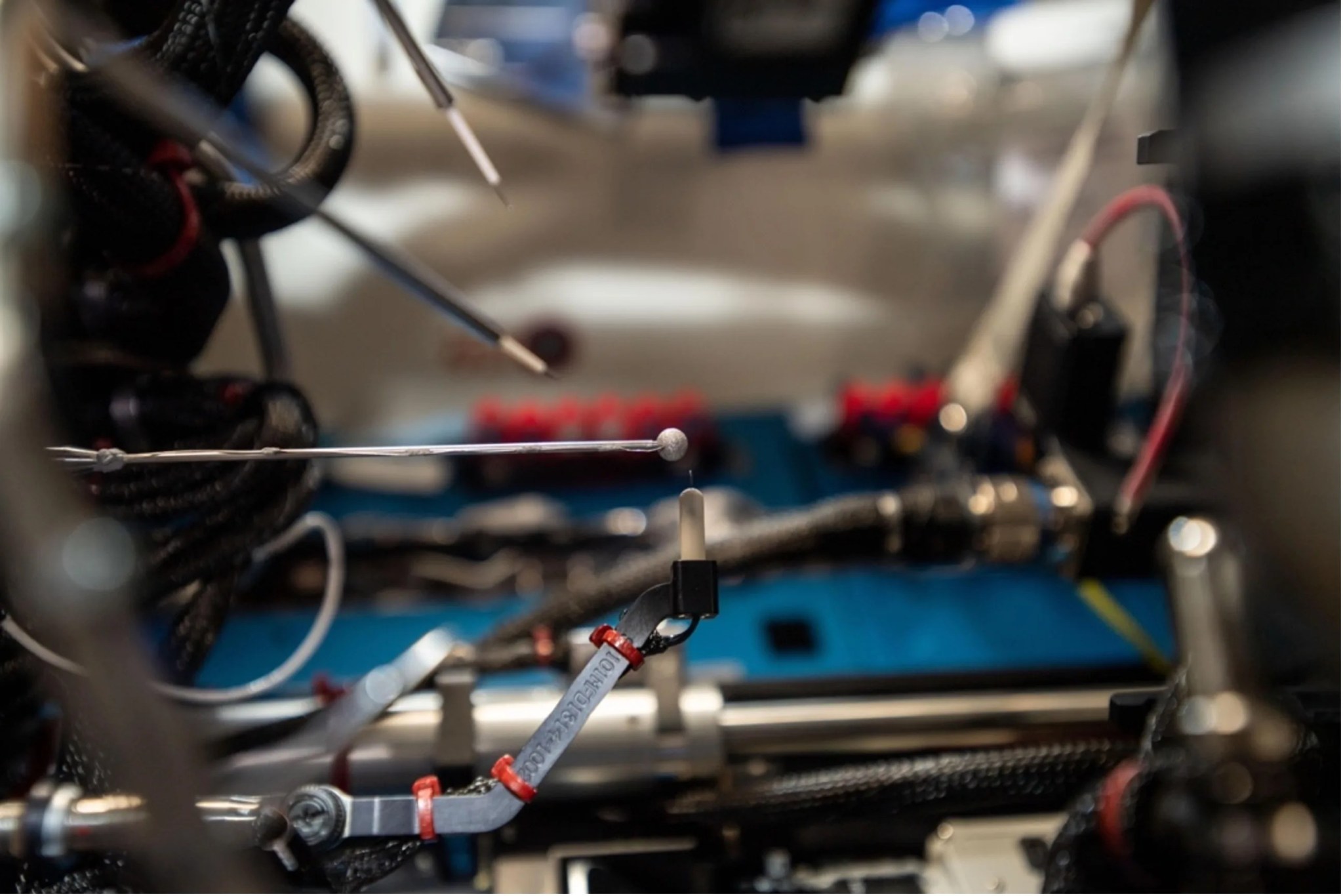 Closeup of mechanical hardware with two pen-like devices in the upper left-land corner, a thin metal rod with a small metallic ball at the tip sticking straight out horizontally from the left, and a thick metal rod underneath with an arm that meets the metallic ball tip.