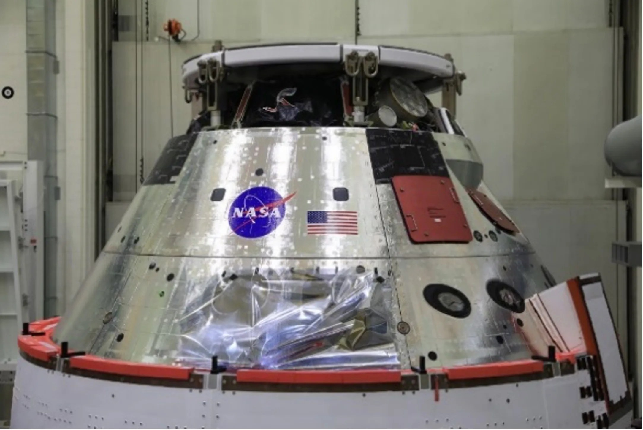 The Orion back shell shines bright with its two rows of silver paneling. The NASA “meatball” insignia and the United States of America flag are affixed to the top row center panel facing the camera. The Orion shell is similar to a three-dimensional cone with the pointed top cut off.