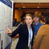 Female high school student pointing at poster board of scientific project