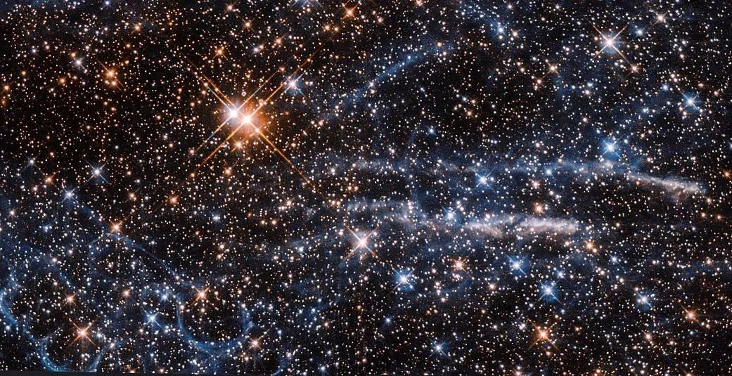 Orange-white and bluish-white stars litter the black background.  Light blue cloud wisps and thicker white clouds across the bottom half of the image.