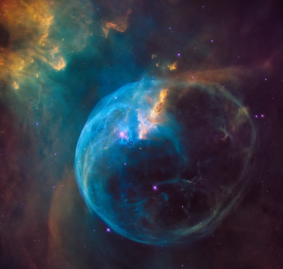 A bubble of blueish gas expands in the lower center of the image. Gas and dust in yellow, green, and brown hues fills the rest of the image.