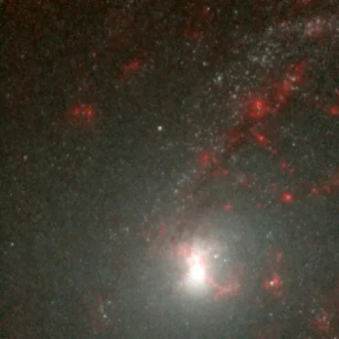 Closeup shot of bright white core of galaxy. Surrounded by red dust and gas.