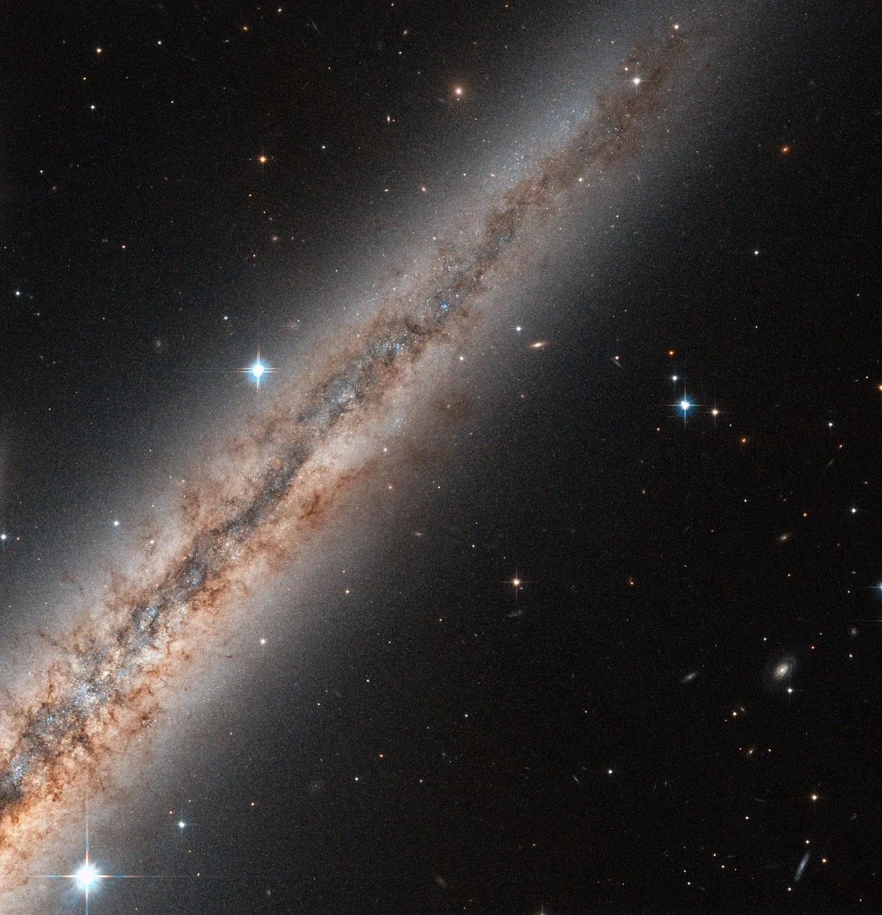 Thin line of stars and dust and gas, the side view of a galaxy. This galaxy is diagonal across the image, with the blackness of space behind it.