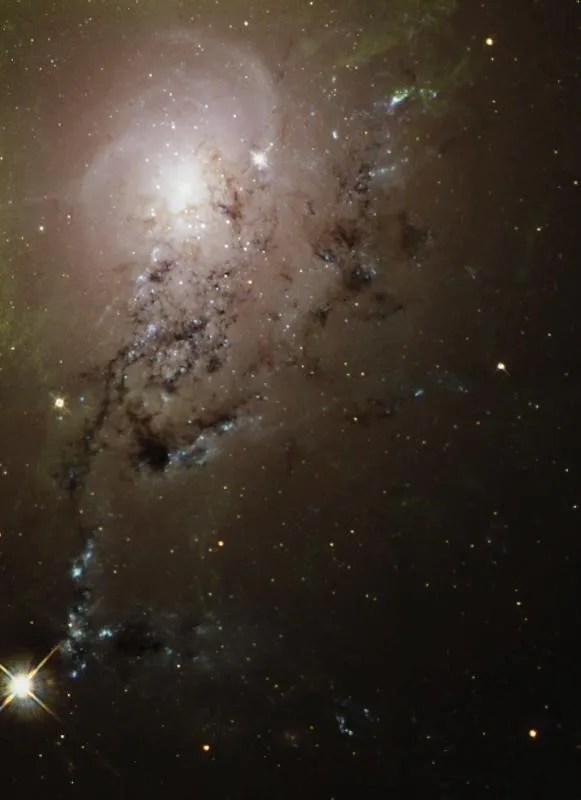 Large glob of white light in the upper left of the image. Surrounded by dark dust and gas.