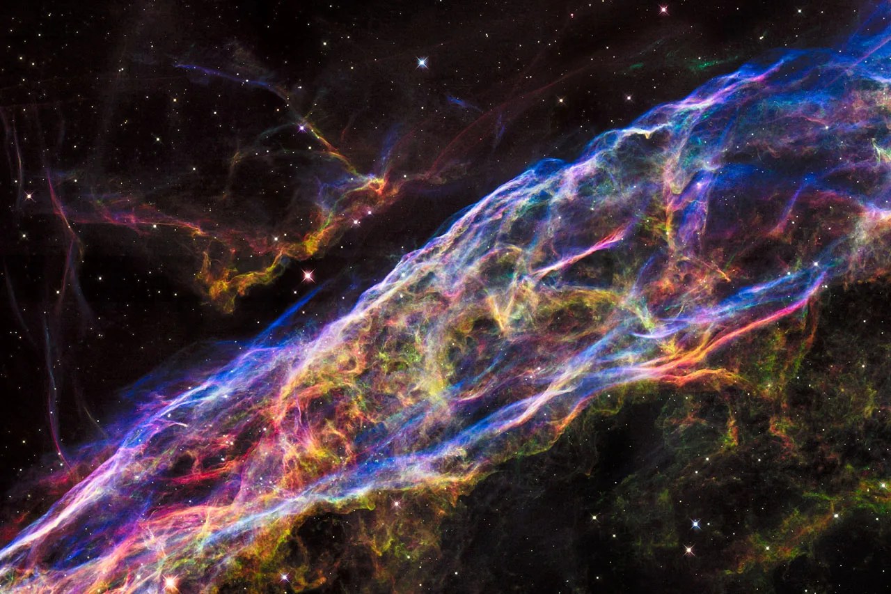 A colorful rainbow chain of gas and dust stretches across the image from the lower left corner to the upper right.