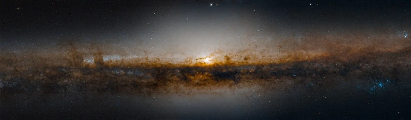 Thin side view of a galaxy, surrounded by dark plumes of gas and dust, blocking most of the stars on the outer edges. But in the center, a bright white light which is the core of the galaxy.