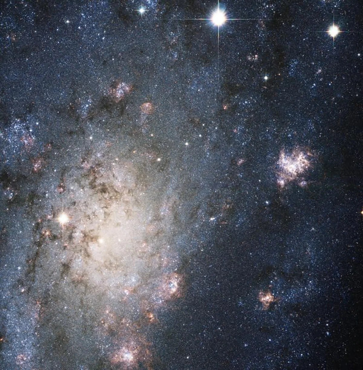 Large grouping of stars within a galaxy center, surrounded by light blue dust and gas