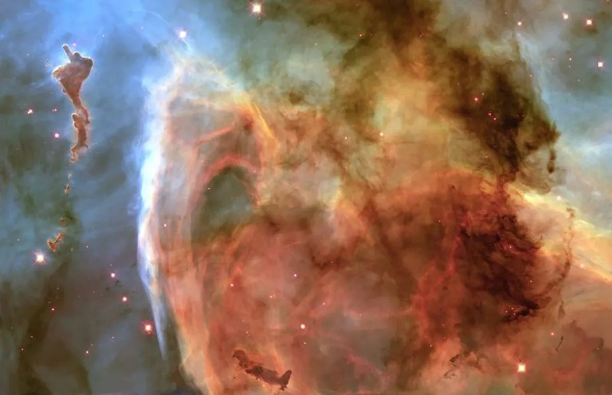 Most of the image is filled with a large, glowing gold and pink to reddish-brown cloud of gas against a hazy white-gray background with scattered pinkish stars.