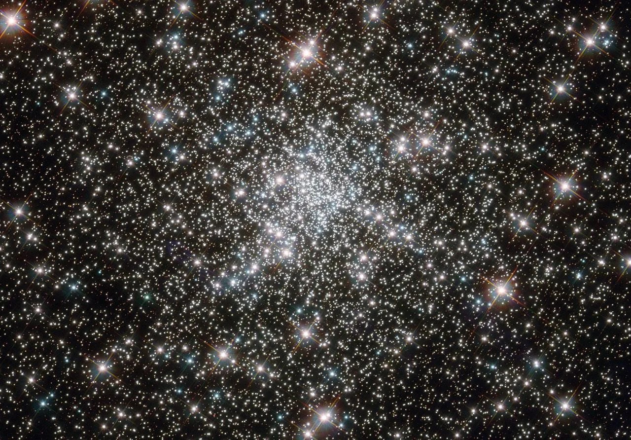 A collection of many white stars against the black background of space. They are more concentrated in the center of the cluster.