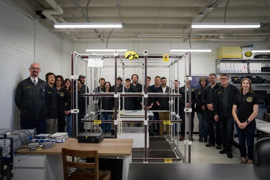 Photograph of 20 people standing in a lab room surrounded by equipment and wearing dark chimera branded clothing.