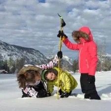 Three people in winter jackets are taking measurements of snow.