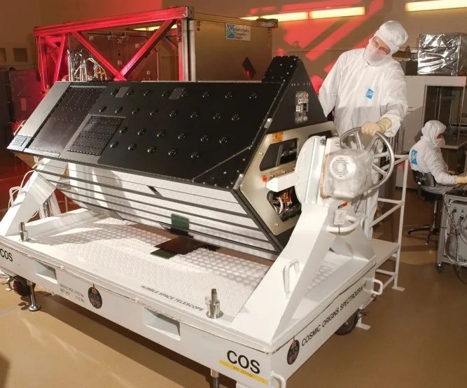 A worker in a white suit stands next to the Cosmic Origins Spectrograph.
