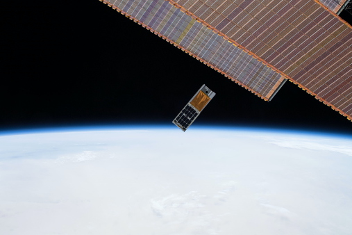 Photo of the HaloSat hardware box after being deployed from the ISS; the ISS solar arrays are to the right with Earth in the background.