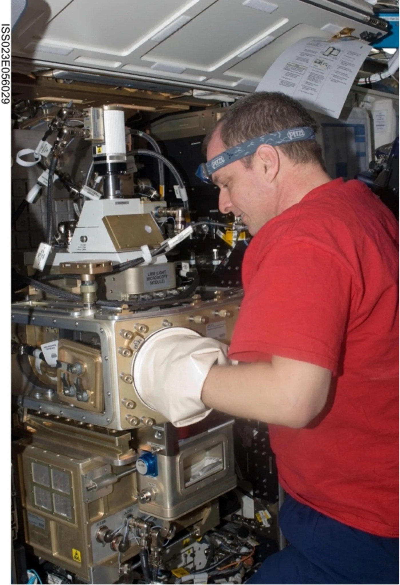 Astronaut with his hand inside a large, white latex glove attached to a gold, mechanical device.