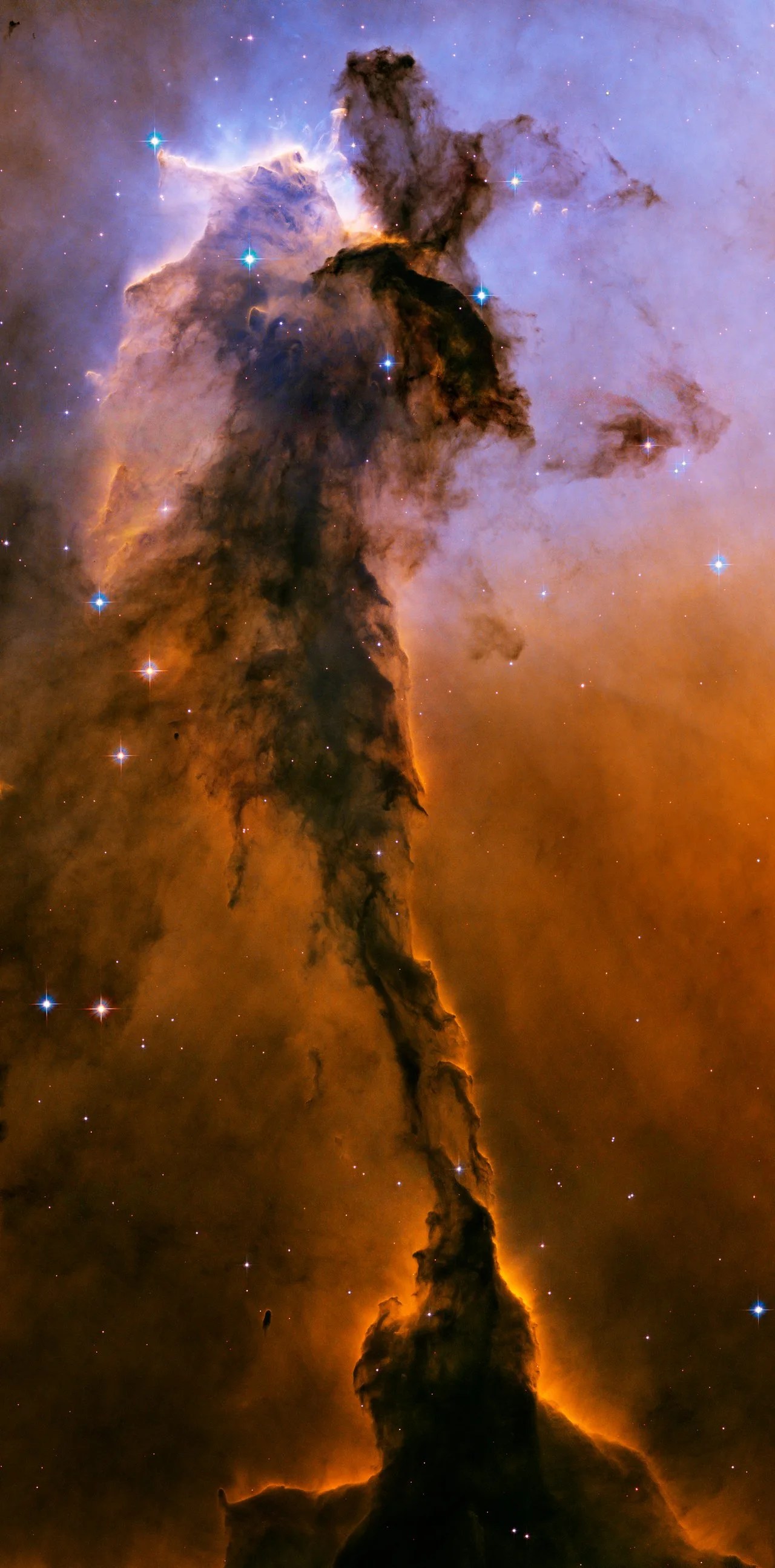 Hubble view of a brownish spire of gas and dust within M16, against a background of mostly red and some blue gas.