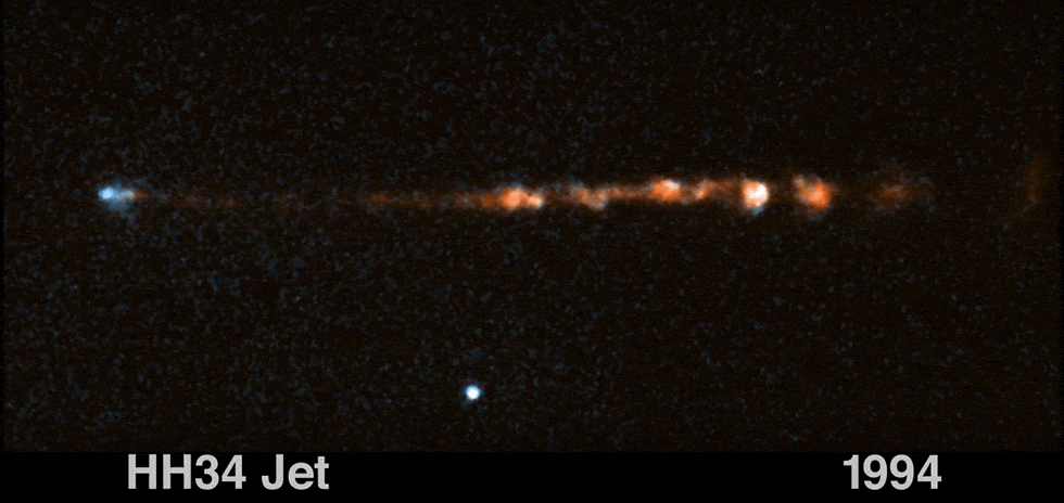 Glowing, clumpy streams of material moving left and right. Left side of the image is a small blue-white cloud slowly moving further to the left. Extending from the blue cloud is a strand of clumpy orange gas moving toward the right. 