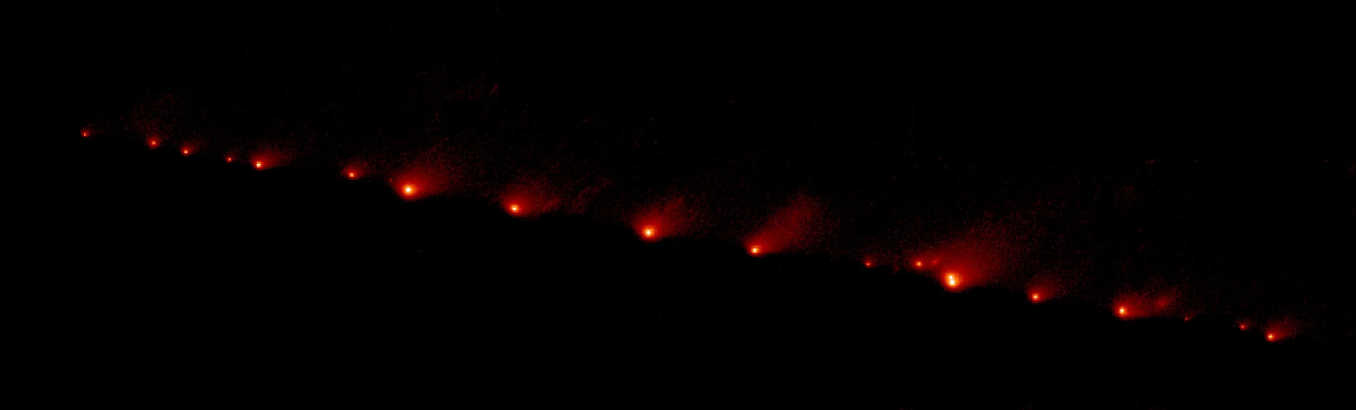 21 blazing fragments of Comet Shoemaker-Levy 9, seen as dark red glints of light against black space.