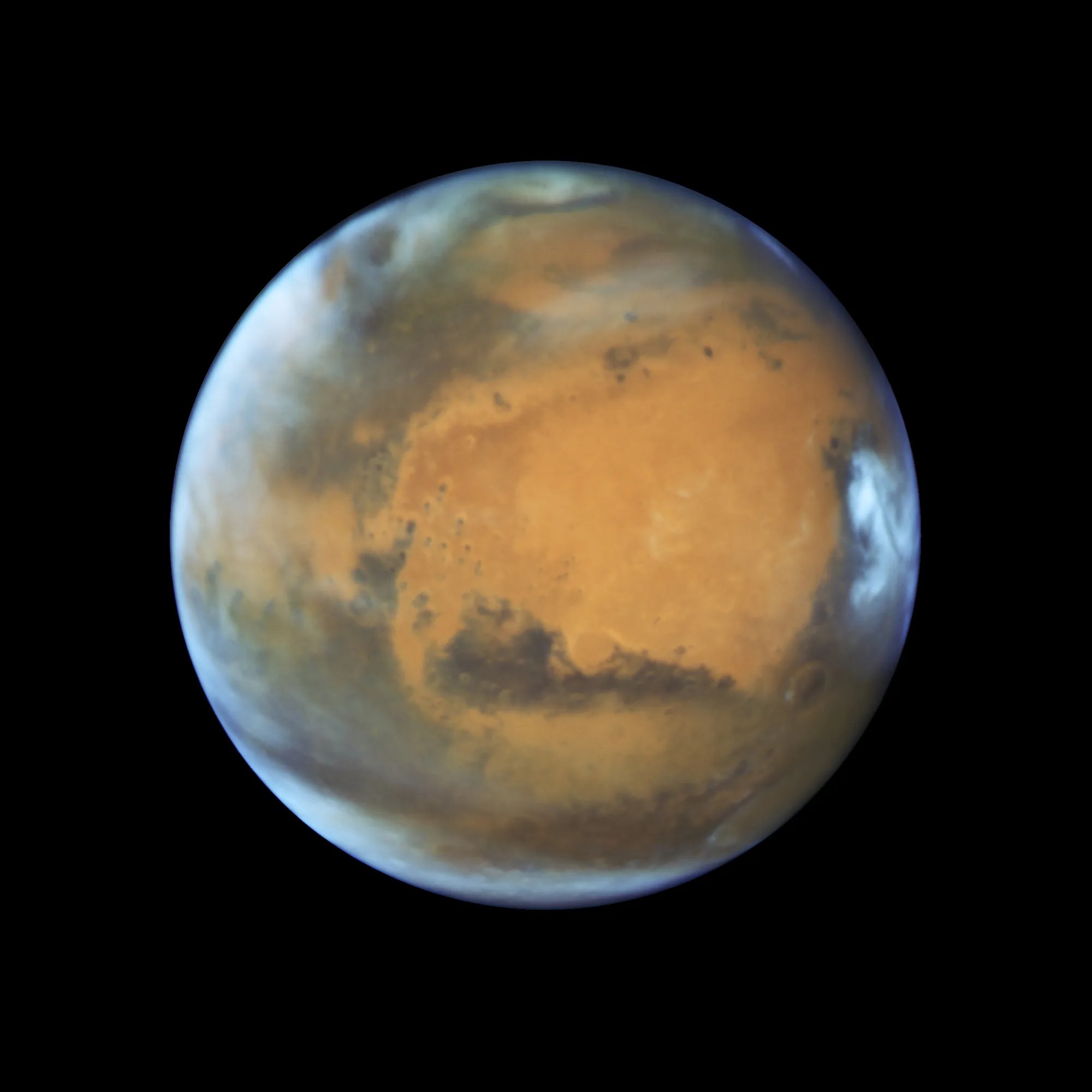 The disk of Mars is set against a black background. The planet is rusty-orange with darker grey areas. Bright-white clouds are visible along the left side of the sphere, and at the poles. An even brighter white patch is visible at the equator of the right limb.