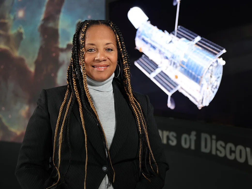 Headshot of Kim Hall standing in front of an Eagle Nebula image and the Hubble Space Telescope image