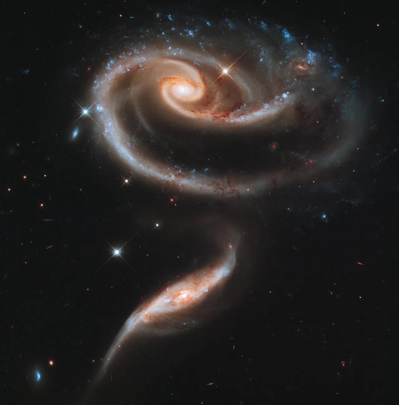 Top: a distorted spiral galaxy. One of its spiral arms extends in a sweeping arc below the galaxy. Below this spiral is another edge-on galaxy extending from the lower left toward image center.