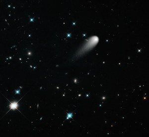 Black background dotted with stars and galaxies. The bright-white comet is in the upper right quadrant of the image, just to the upper right of center. Its tail is pointing toward the lower left corner.