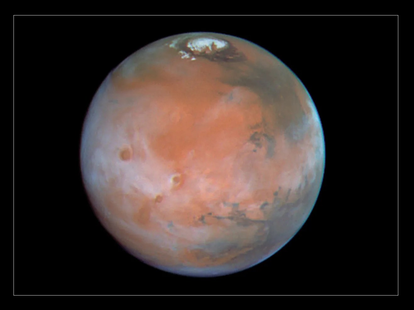 Rusty-red Mars with a haze of white clouds and a white north polar cap.