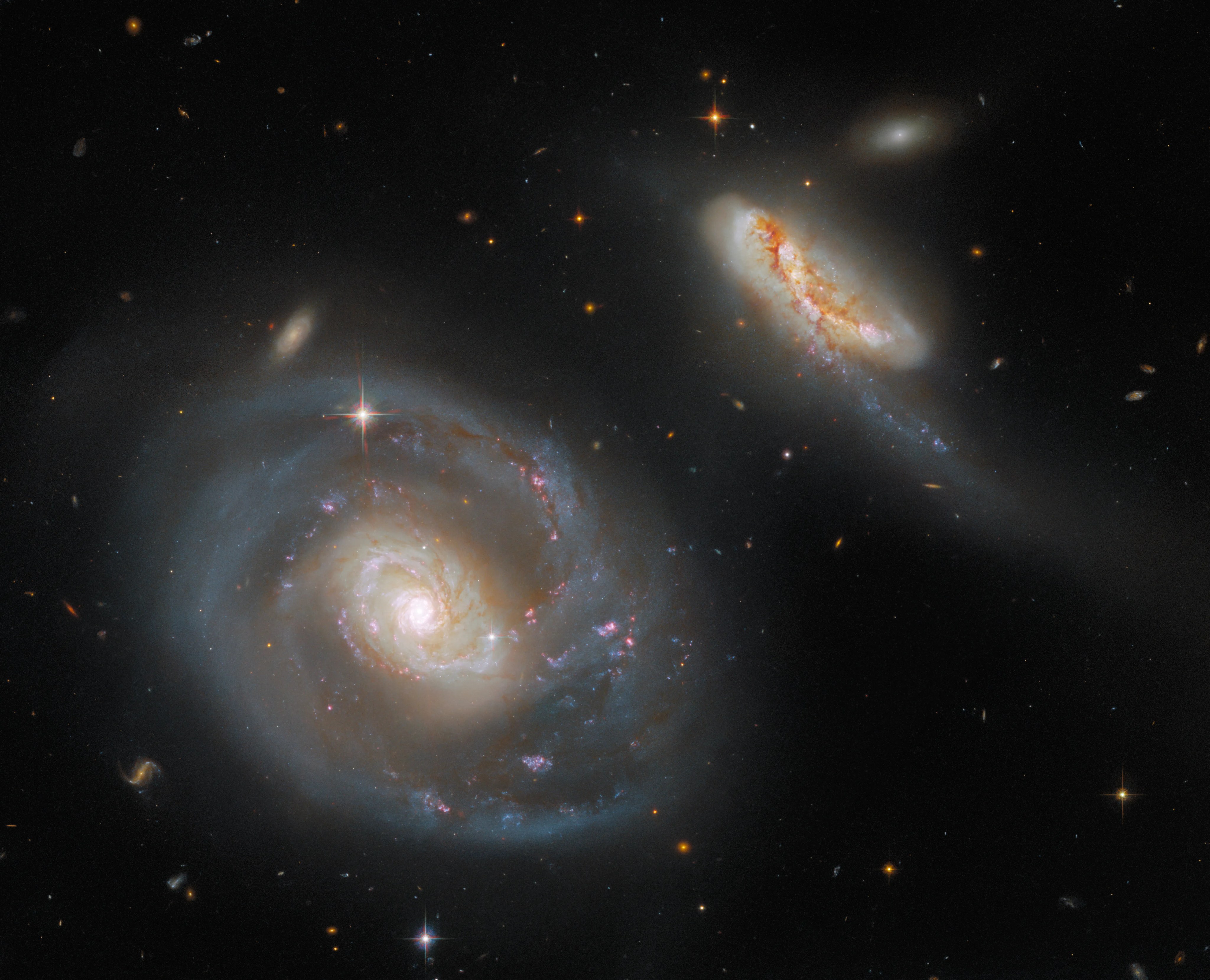 Large face-on spiral galaxy on the lower-left half of the image with a smaller galaxy in the upper left. several smaller galaxies are seen in the background