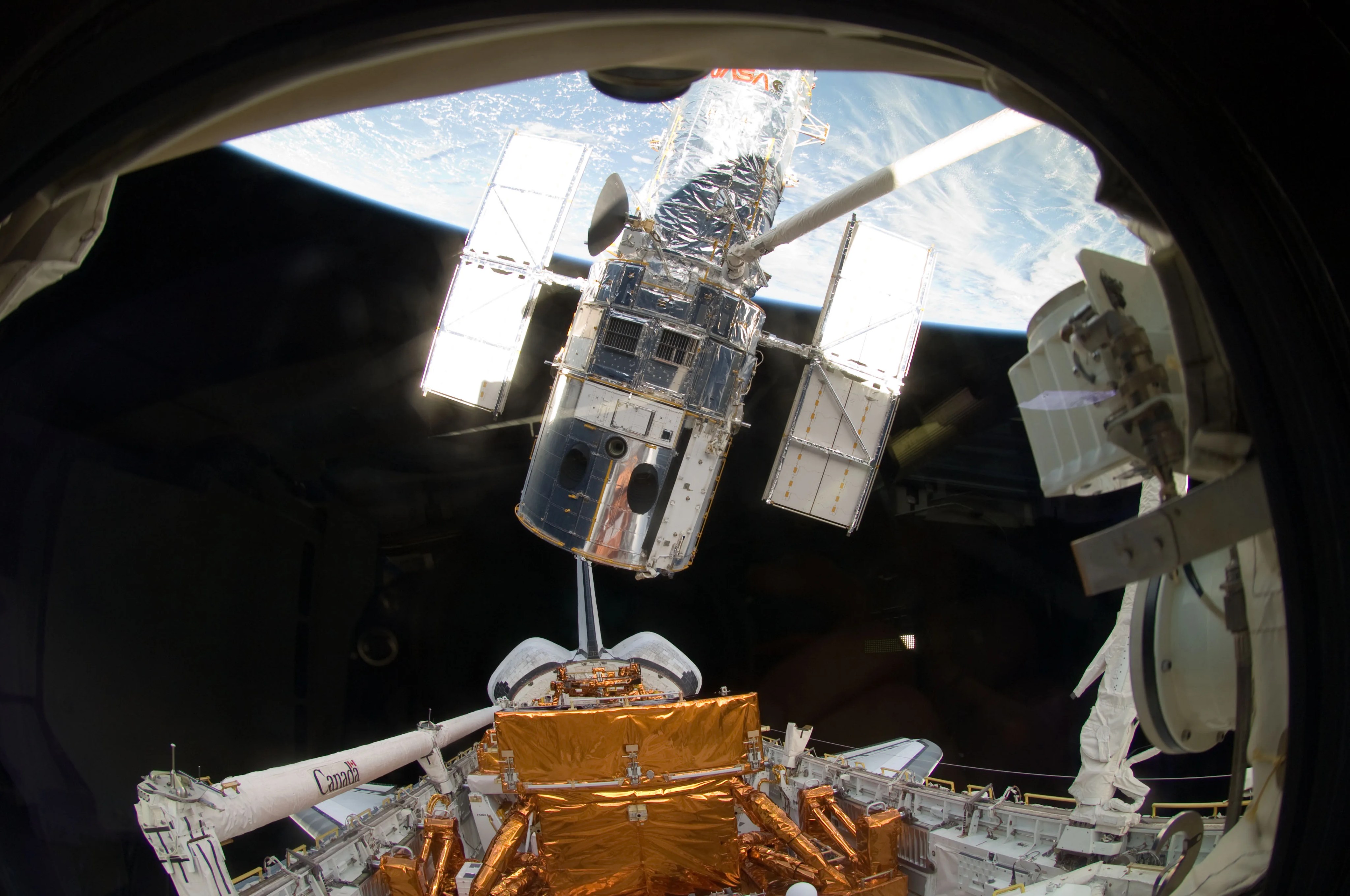 The space shuttle Atlantis' robotic arm lifts Hubble, with Earth visible in the background.