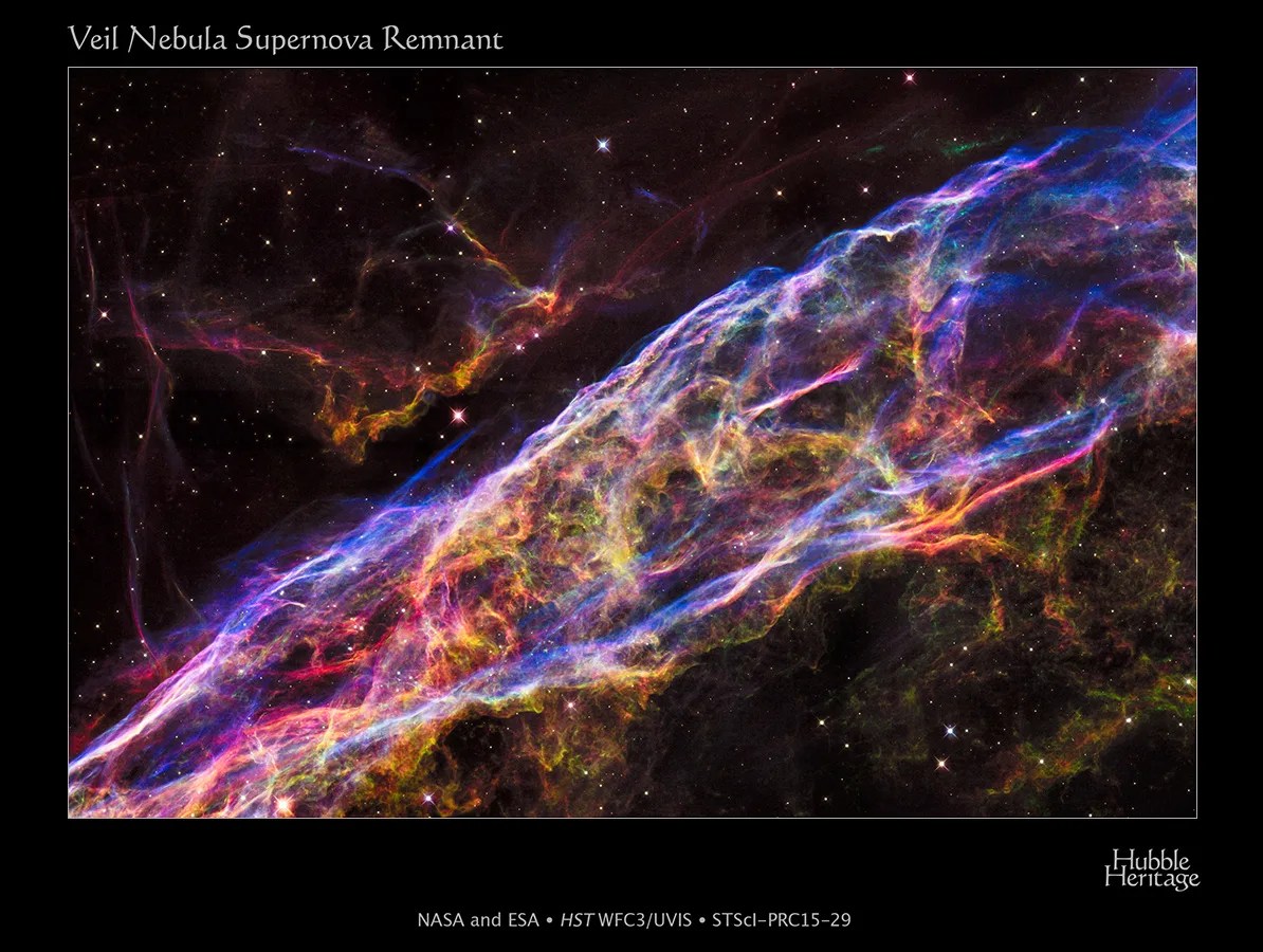 A small section of the Veil Nebula, seen as intricate filaments of pink, purple, green, and yellow gas against black space and dotted with stars.