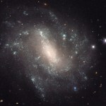 A sparkling galaxy with a bright, glowing core and patchy spiral arms dotted with pale blue star formation.