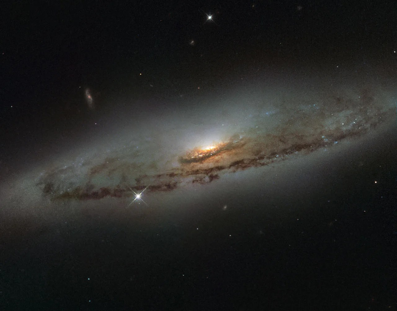 Image of spiral galaxy ngc 4845, a flat and dust-mottled reddish-brown disk surrounding a bright orange galactic bulge.