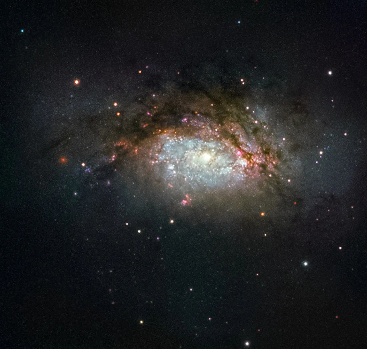 A collision between two good-sized galaxies, slowly evolving to become a giant elliptical galaxy, leaving a glowing center of blue stars, surrounded by pink and red stars and brownish-orange cloud-arms of gas and dust.
