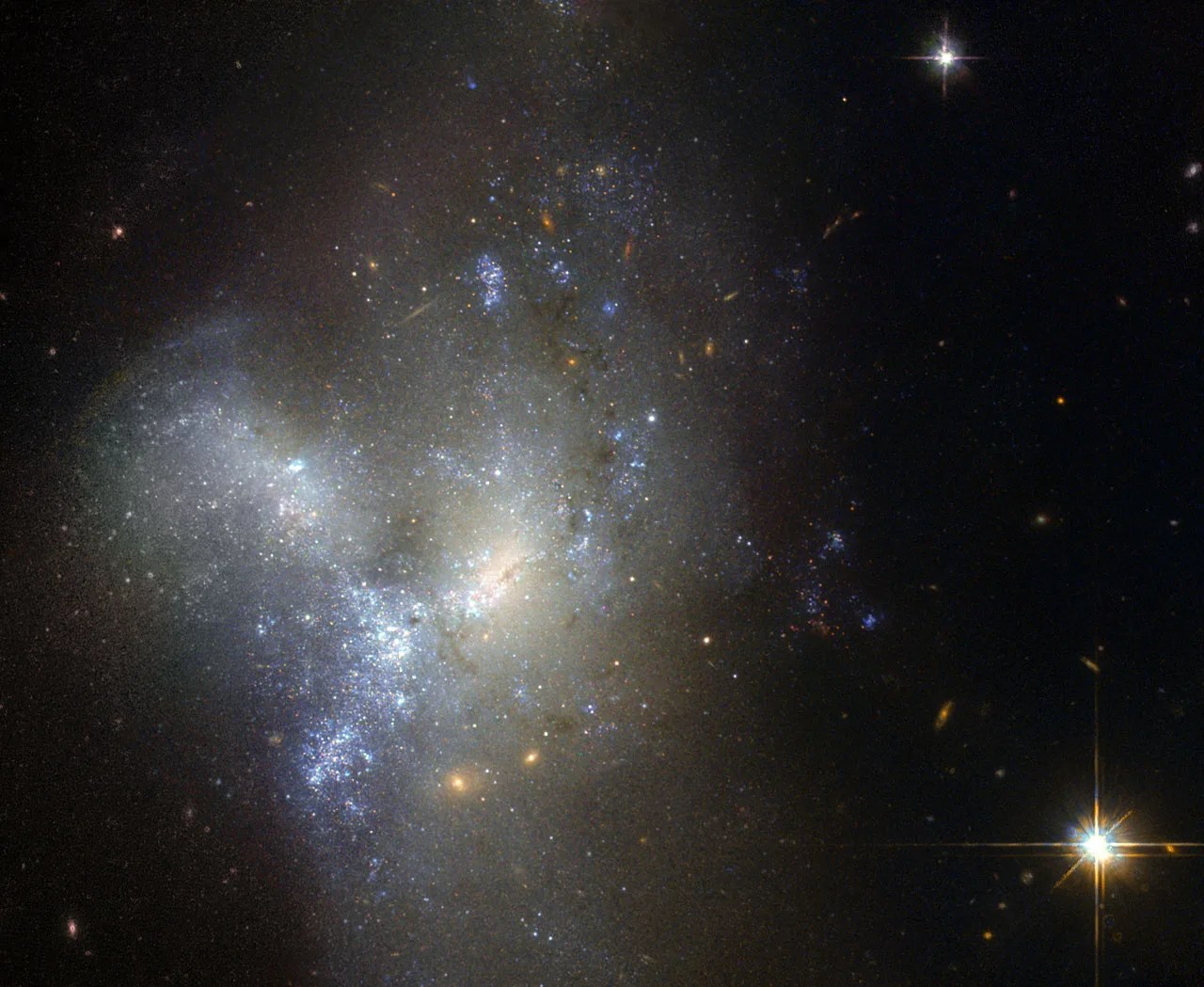 Two or more galaxies are merging together, with a glowing core and surrounded by a grayish haze of gas and many bright blue stars.