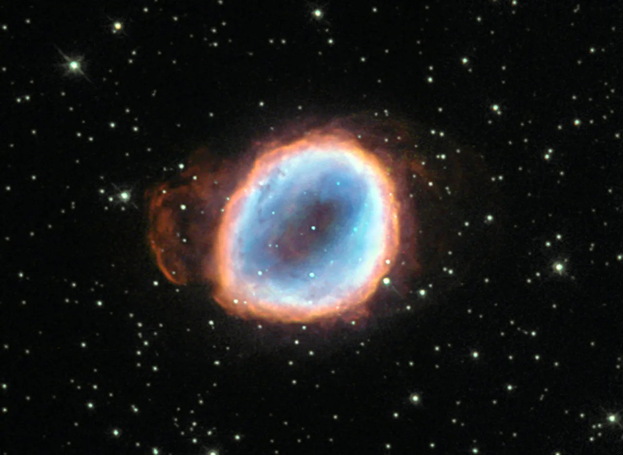 A dying star's remains are seen as a roughly circular region of gas, with an inner teal region and orange at the edges, all against black space dotted with stars.