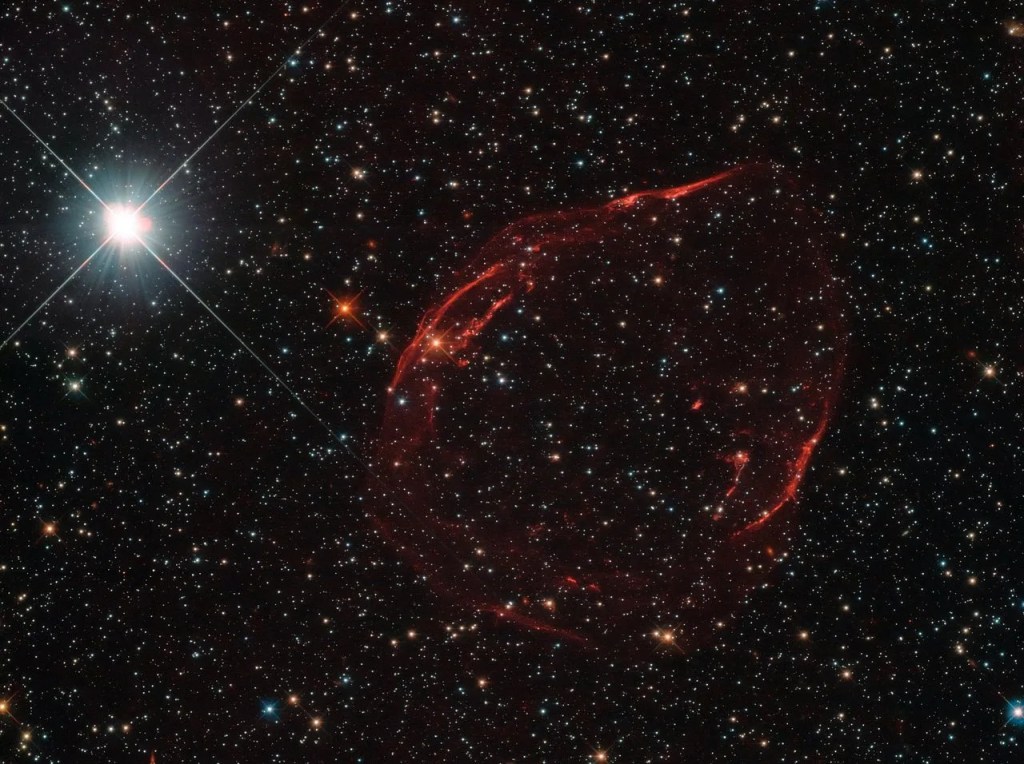 A c-shaped red "whisp", leftover shrapnel of a dead star. In the upper left corner is a bright white star.