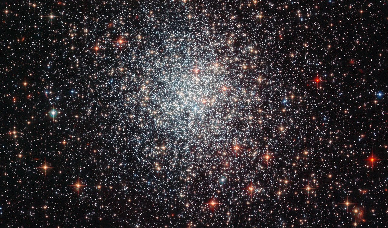 A spherical cluster of white, red and some blue stars, thicker and denser toward the center,