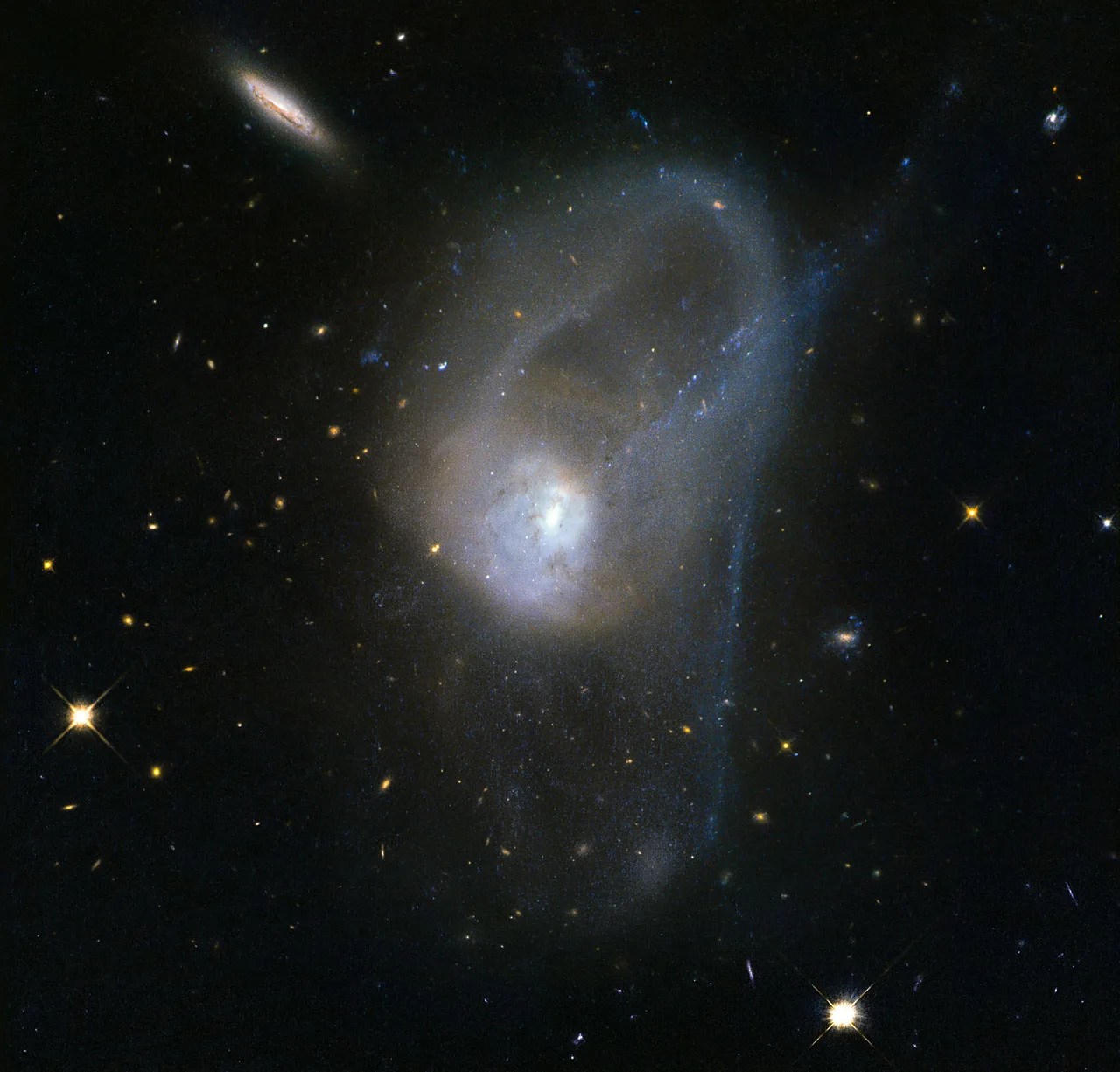 Pair of interacting galaxies merging, seen as a bright white central region of light surrounded by hazy trails of stars.