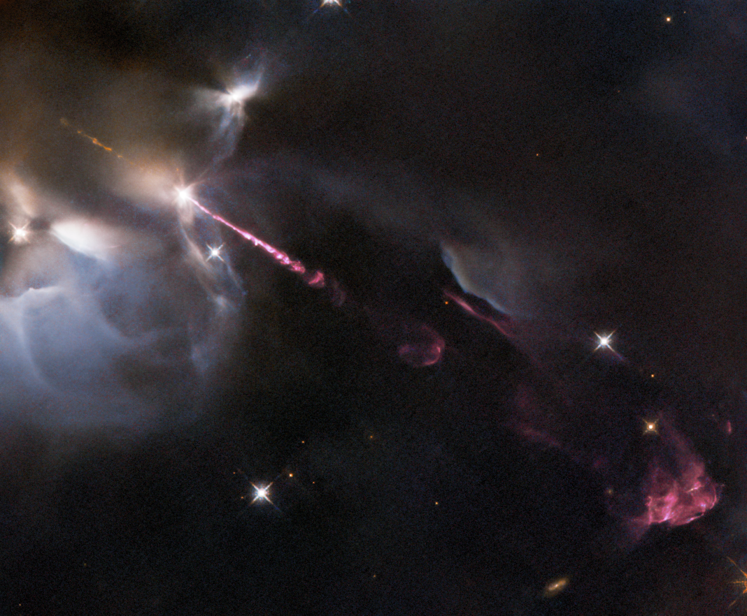 Dark cloud of gas and dust a with bright-white glowing outline in the upper left. pinkish-red jet of material extends from the cloud to the lower right where billowing reddish-pink cloud forms. background stars