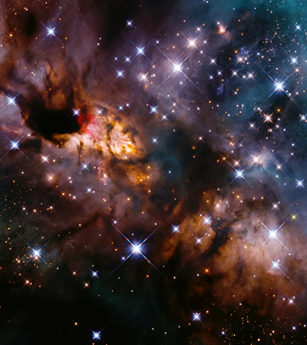 Dark dust lanes and clumps block the light from bright white, red, and rust-colored clouds that stretch diagonally across the image. blue-white stars fill the upper right