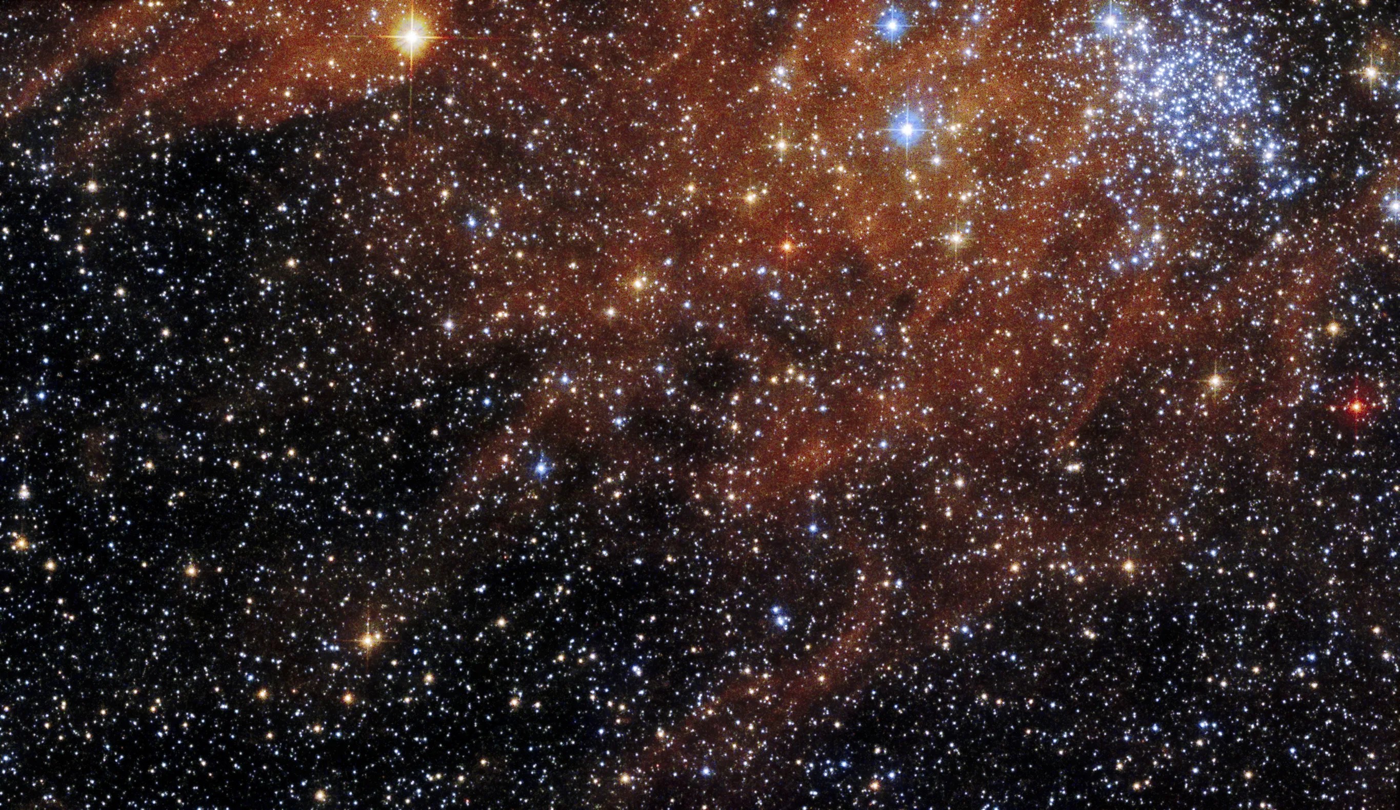 Bright blue-white cluster of stars at upper right, surrounded by field of dimmer stars and rusty-red gas and dust clouds