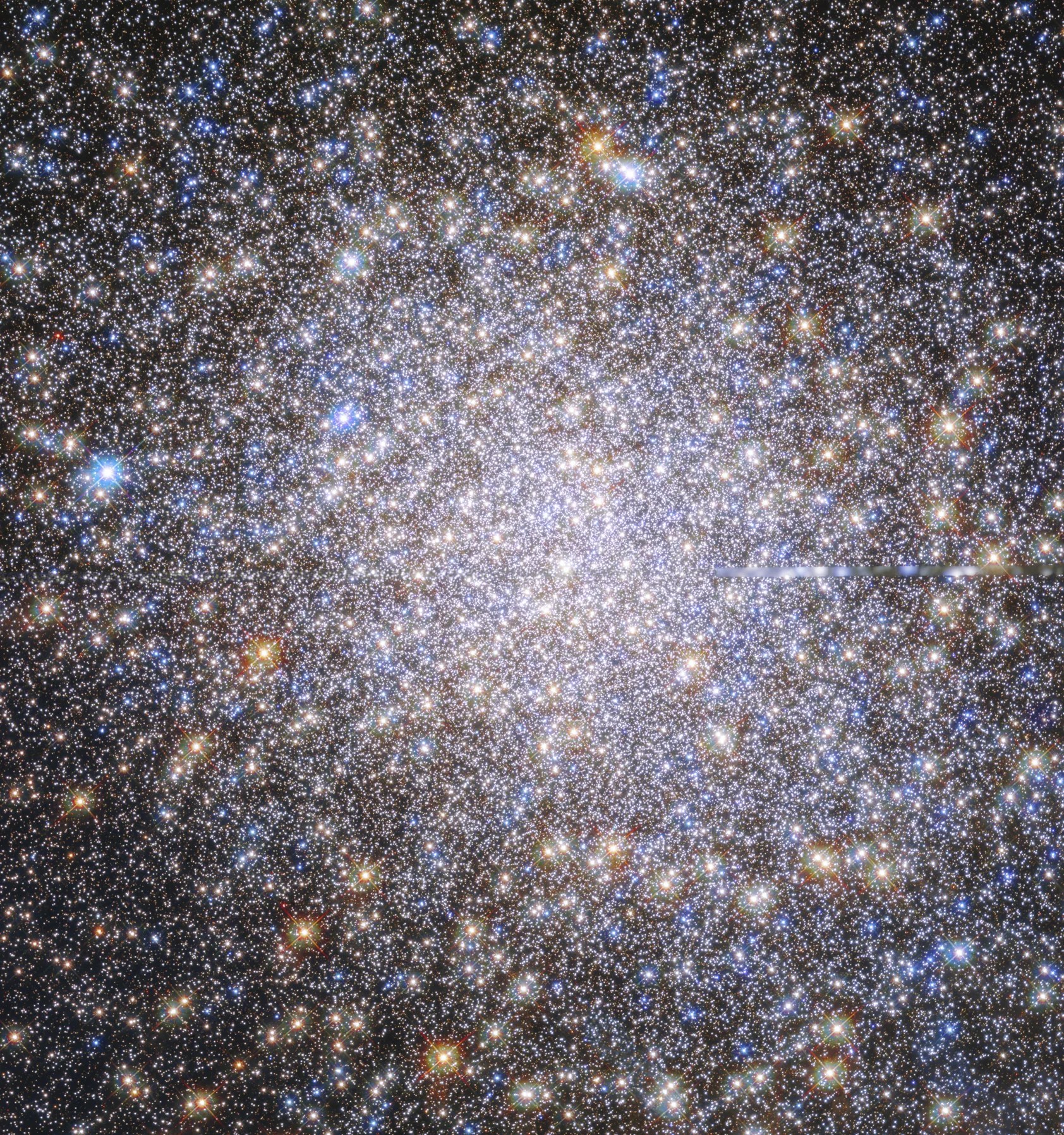 The field is filled with orange, red, yellow, blue, and white stars. They appear as a spherical, dense mass that tapers out toward the edges of the image on a black background.